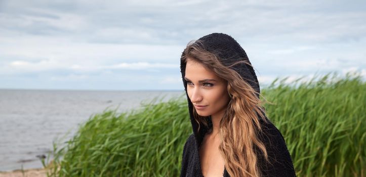 Portrait of an young woman in a black sweater on a cold day on the beach
