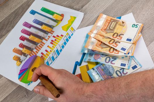 man hand holding cigar near 50 and 20 euro in statistics background