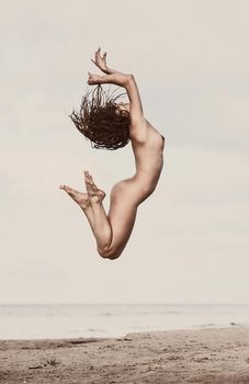 Young nude woman jumping on the beach. Old photo stylization, film grain added