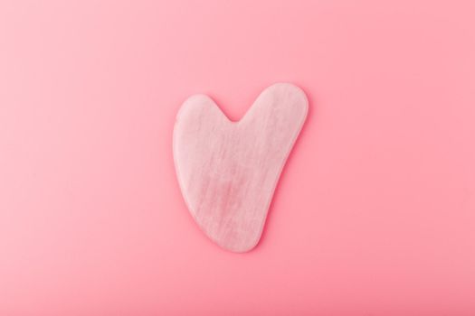 Top view of pink heart shaped guasha stone made of quartz crystal on bright pink background. Concept of alternative skin care treatment, self massage and acupressure