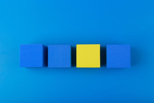 Creative flat lay with three blue and one yellow blocks in a row against blue background. Concept of individuality and identity