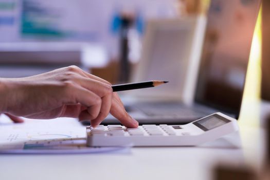 Close up, Businessman or Professional Entrepreneurship holding a pencil and press calculator with the laptop,  paper report, income graph.