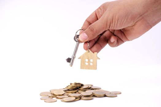 Hand holding house key on money coin stack and white isolated background.