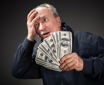 Confused elderly man with fan of dollars