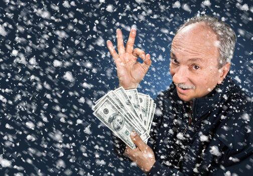 Time to buy gifts. Portrait of a man with a bundle of dollars on a blue background in snowfall