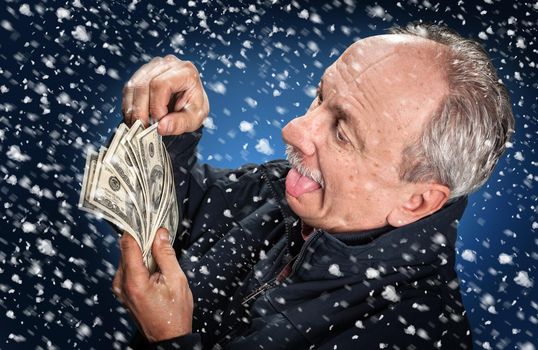 Time to buy gifts. Portrait of a man with a bundle of dollars on a blue background in snowfall