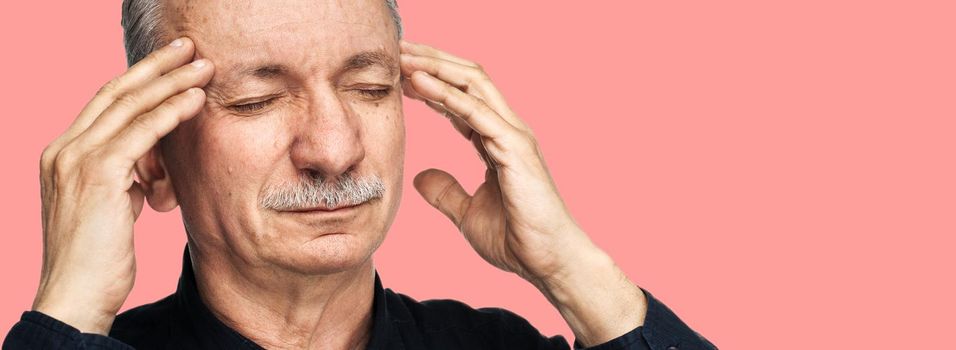 Strong headache. Old man touches his head with his hands and feeling tired and headache. Health care concept. Old man suffering from a headache isolated on pink background with copy space.
