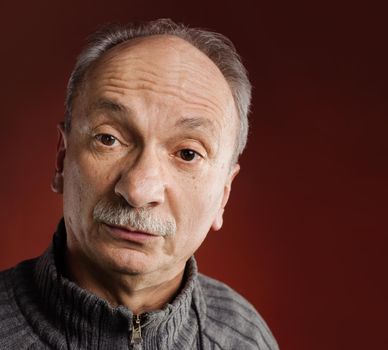 Feeling confused. Portrait of a surprised elderly man on red background