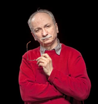Portrait of an thoughtful elderly man with glasses in his hands on a dark background