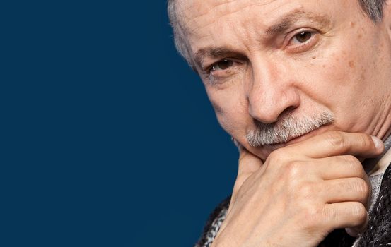 Portrait of handsome senior man prop up the head with his hand on blue background with copy-space