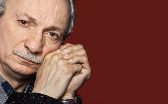 Handsome senior man with a skeptical expression on dark red background with copy-space