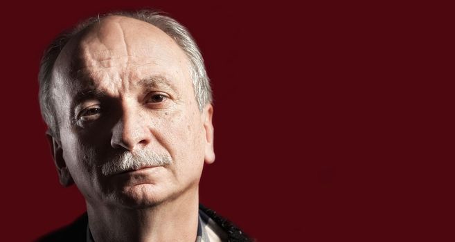 Portrait of handsome senior man with a tired expression on red background with copy-space