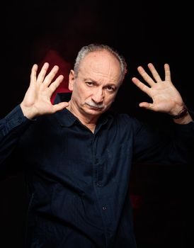 Portrait of elderly man with hands up on a dark background