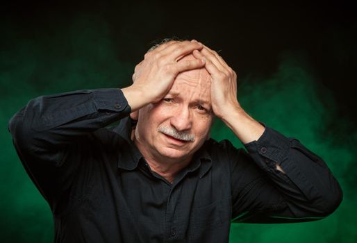 Headache. An elderly man holding head in his hands
