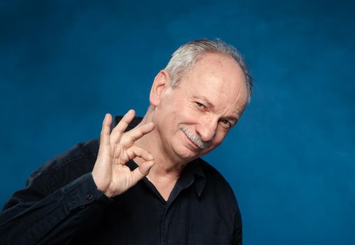 Happy elderly man showing ok sign on a blue background