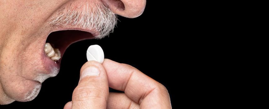 Close-up image of an old man wants to take a pill isolated on black background with copy-space