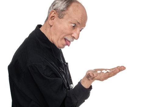 Medicine and health concept. Elderly man with bulging eyes and protruding tongue with pills in hands on a white background. Old man wants to take a pill