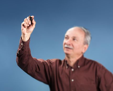Old man holding a orange marker on blue background. Focus on hand