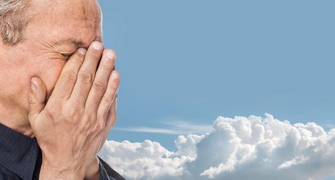 Portrait of an elderly man with face closed by hand on blue cloudy sky