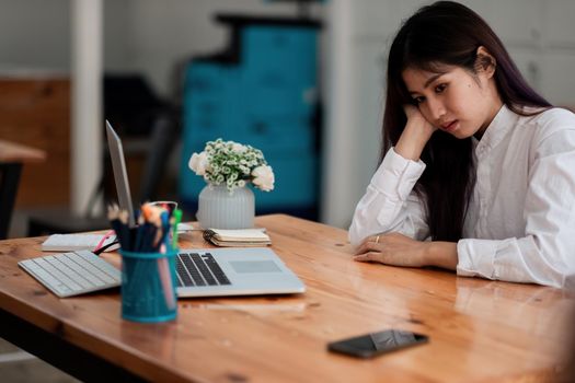Bored asian female worker lie at office desk look at mobile phone and laptop screen think about problem solution, unmotivated businesswoman search inspiration, tired of monotonous work. Lack of motivation concept
