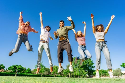 Group of happy young diverse multiracial gen z friends jumping together raising arms and legs looking to the camera. Concept of success and living the nature to a better healthy natural life