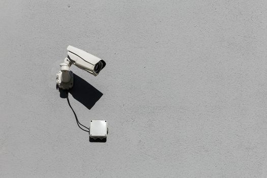 small white surveillance camera on flat gray matte plaster wall pointing sideways