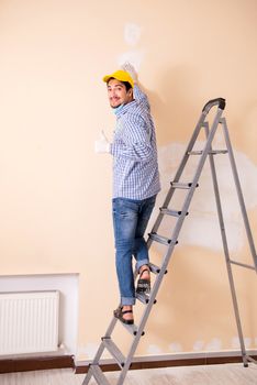 Young contractor sanding wall down with sandpaper 