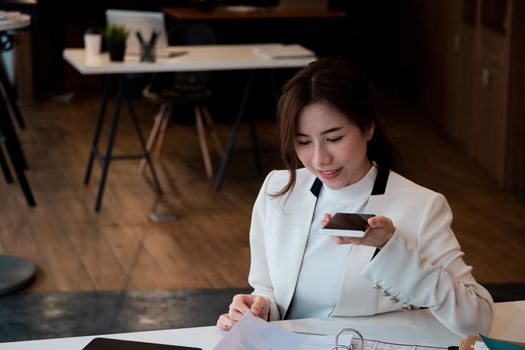 Young asian businesswoman beautiful charming smiling and talking on the mobile phone with speaker phone in the office.