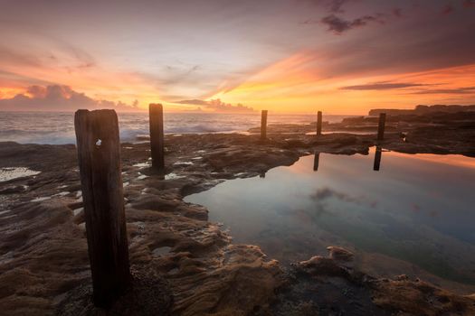 Soft diffused sunrise light and light sea fog at old coastal rock pool.  focus to first timber post. Beautiful colours begin to colour in the clouds.