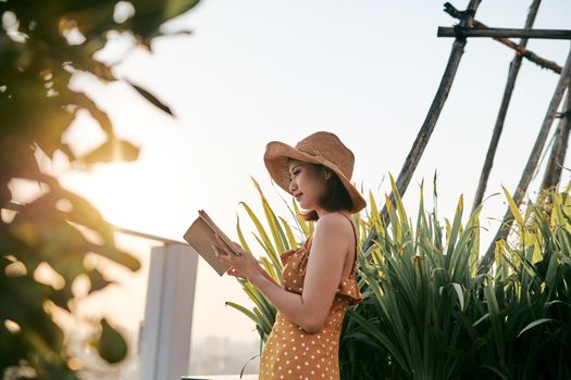 Young Asian girl reading in nature under summer sunshine
