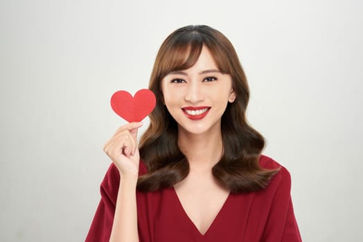Pretty young Asian woman holding white paper heart and smiling happily at camera