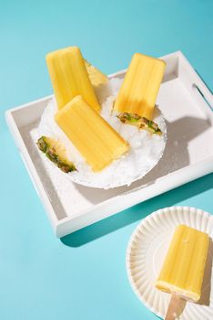 Pineapple ice pops on a tray. Top view scene over a blue background