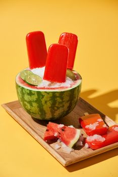 Watermelon popsicle and sliced watermelon on wood tray top view