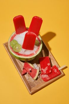 Summer mood, watermelon popsicle and sliced watermelon on wood tray over yellow background