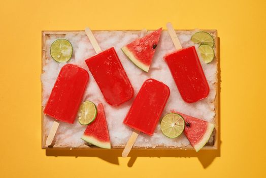 Watermelon popsicles and sliced lemon on ice filled tray 