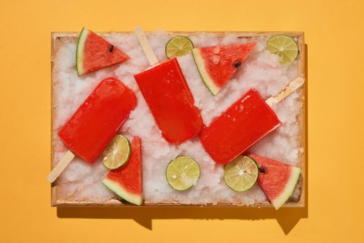 Watermelon popsicles and sliced lemon on ice filled tray 