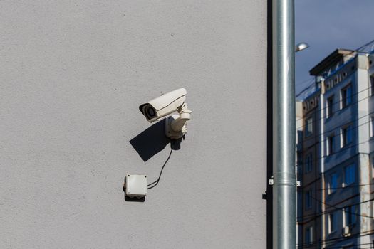 small white surveillance camera on flat gray matte plaster wall in city pointing sideways