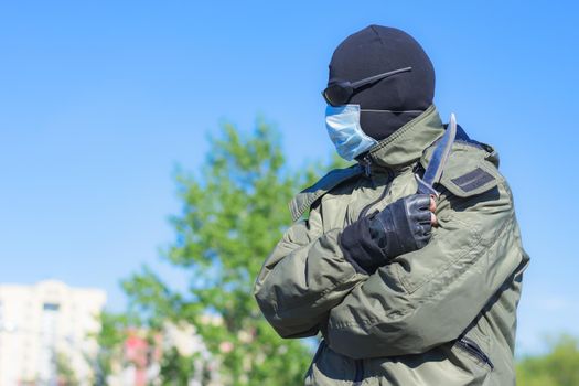 Modern dangerous and armed criminal in balaclava and medical mask among city streets