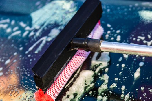 Washing and cleaning the front window of a car with mop in self service car wash station, close up isolated.