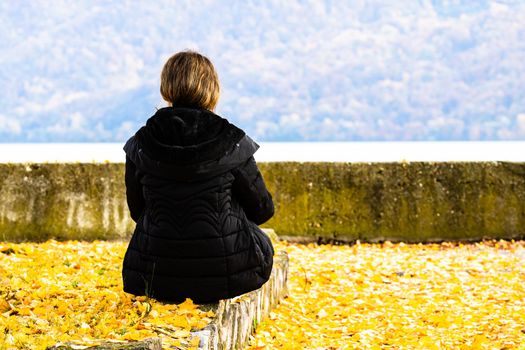 Autumn leaves fallen on standing alone woman on the autumn alley. Autumn landscape, orange foliage in a park in Orsova, Romania, 2020