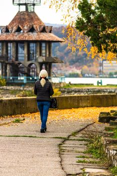 Alone woman walking on the autumn alley. Autumn landscape, orange foliage in a park in Orsova, Romania, 2020