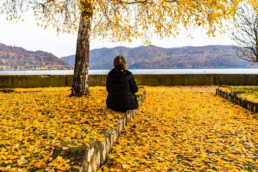 Autumn leaves fallen on standing alone woman on the autumn alley. Autumn landscape, orange foliage in a park in Orsova, Romania, 2020