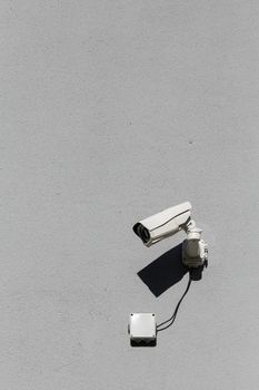 small white surveillance camera on flat gray matte plaster wall pointing sideways