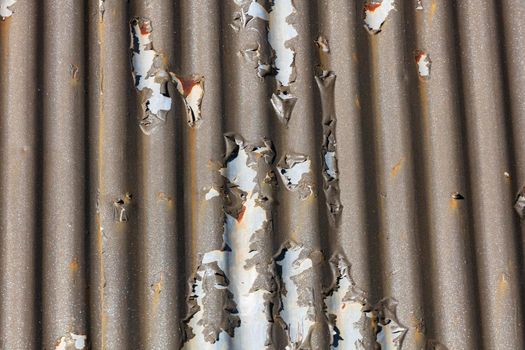 Photograph of brown paint peeling off a corrugated iron roof due to exposure to the environment