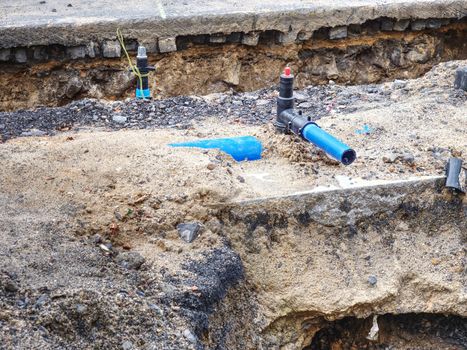 Blue steel water branch pipe installation in excavated trench in bright light.