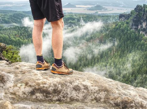 Hiker legs climbing on sunrise mountain peak rock. Slim  legs of a mountain hiker with hiking boots on exposed rock.