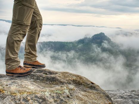 Traveler or hiker legs in sports wearing. View over verdant valley, low clouds.