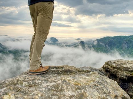 Traveler or hiker legs in sports wearing. View over verdant valley, low clouds.