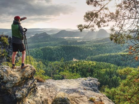 Photographer or videographer  traveler with heavy backpack and tripod in hand is preparing for art work. Artist in pure nature take impressive landscape photos.