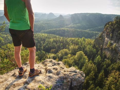 Tall runner in green singlet and black pants. Fearless boy at edge. Rocky peak at sunrise.